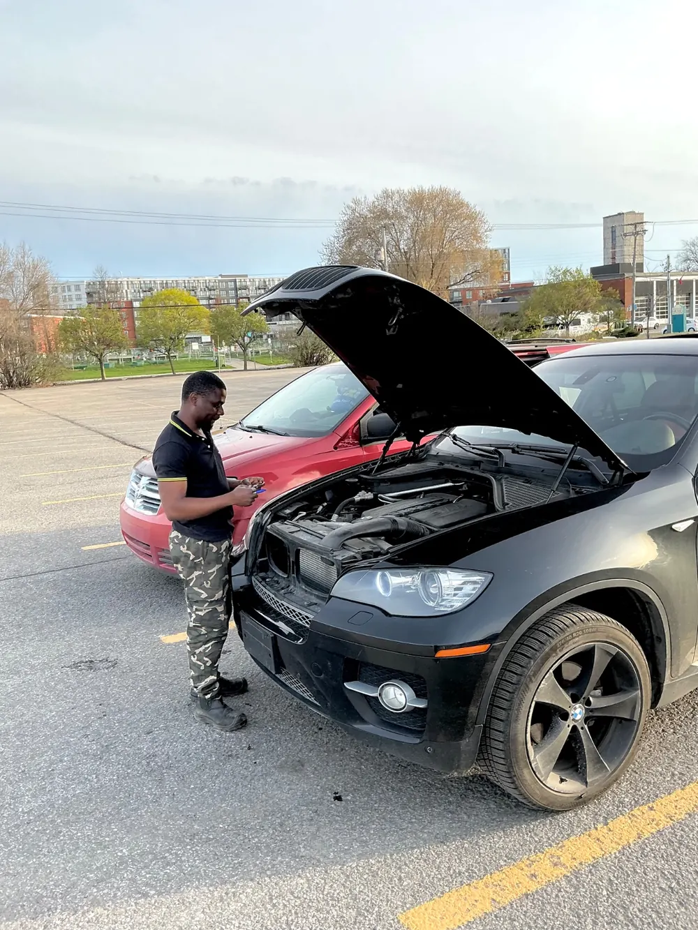 Elie, founder of Auto Service Alimotorsforall, diagnosing a black BMW X6 with the hood open