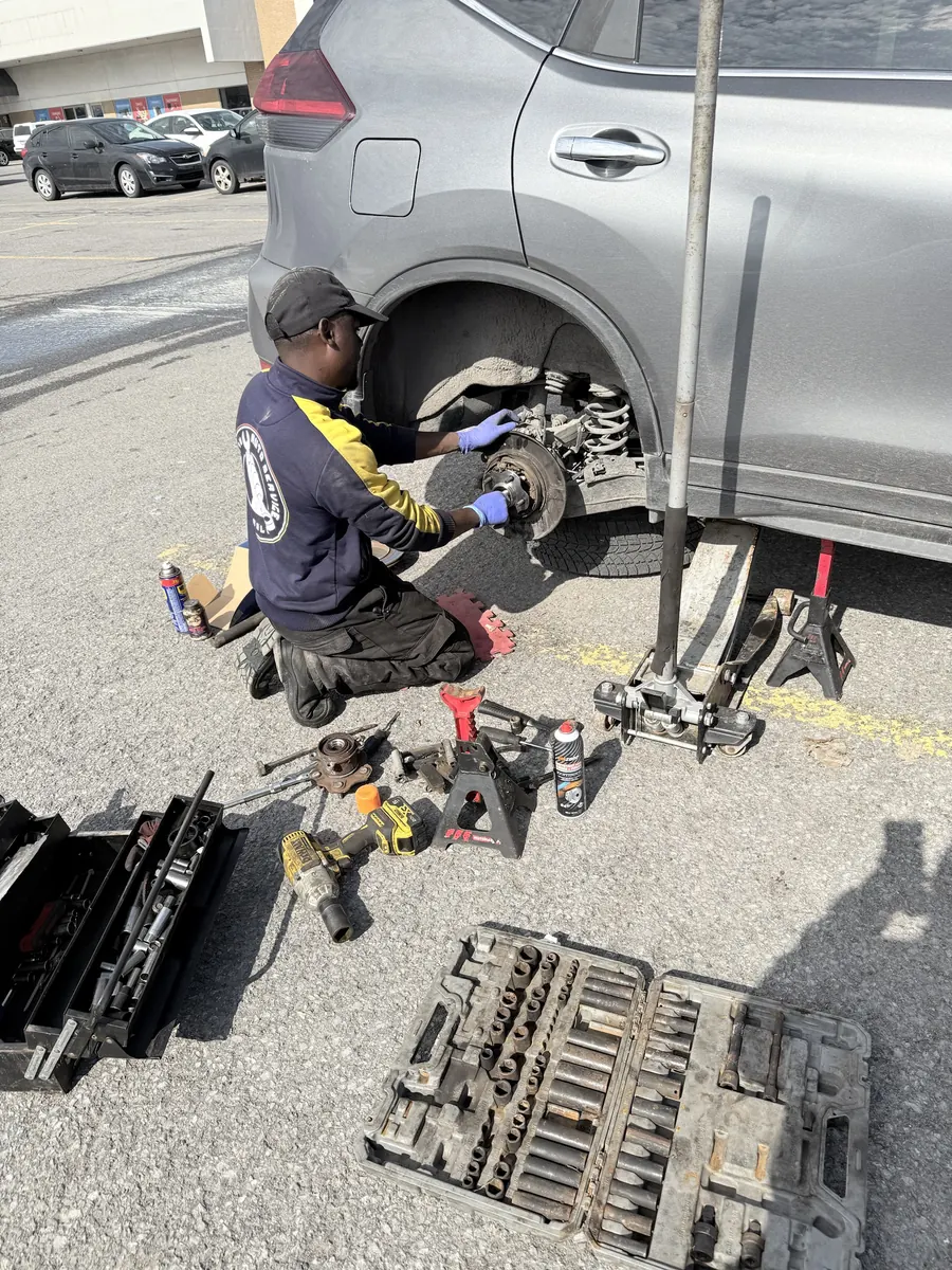 Elie working at the rear hub of a grey Nissan Rogue on jack stands, tools laid out